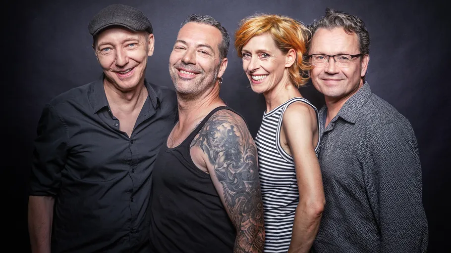 Four people smiling, posing against dark background.