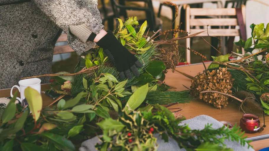 Person assembling wreath with various greenery.