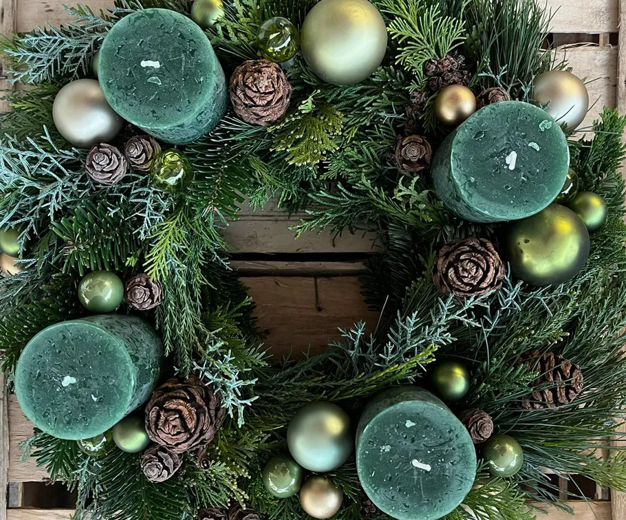 Green wreath with candles and pinecones on wood.