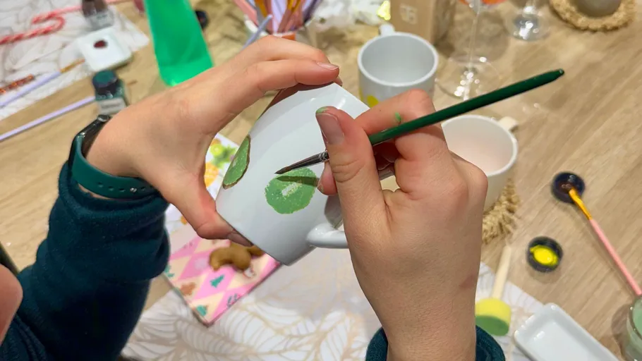 Hands painting green patterns on white mug.