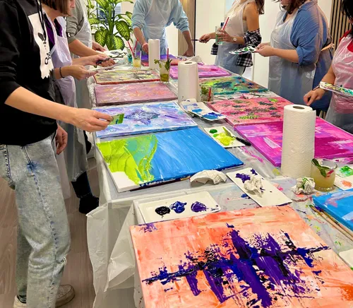 People painting colorful canvases on long table.