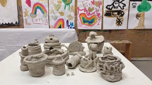Clay sculptures on table, colorful paintings behind.