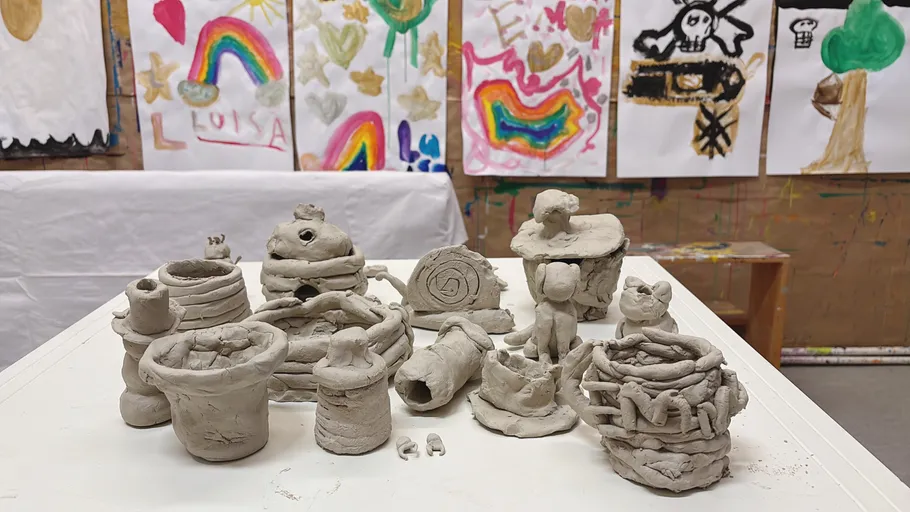 Clay sculptures on table, colorful paintings behind.