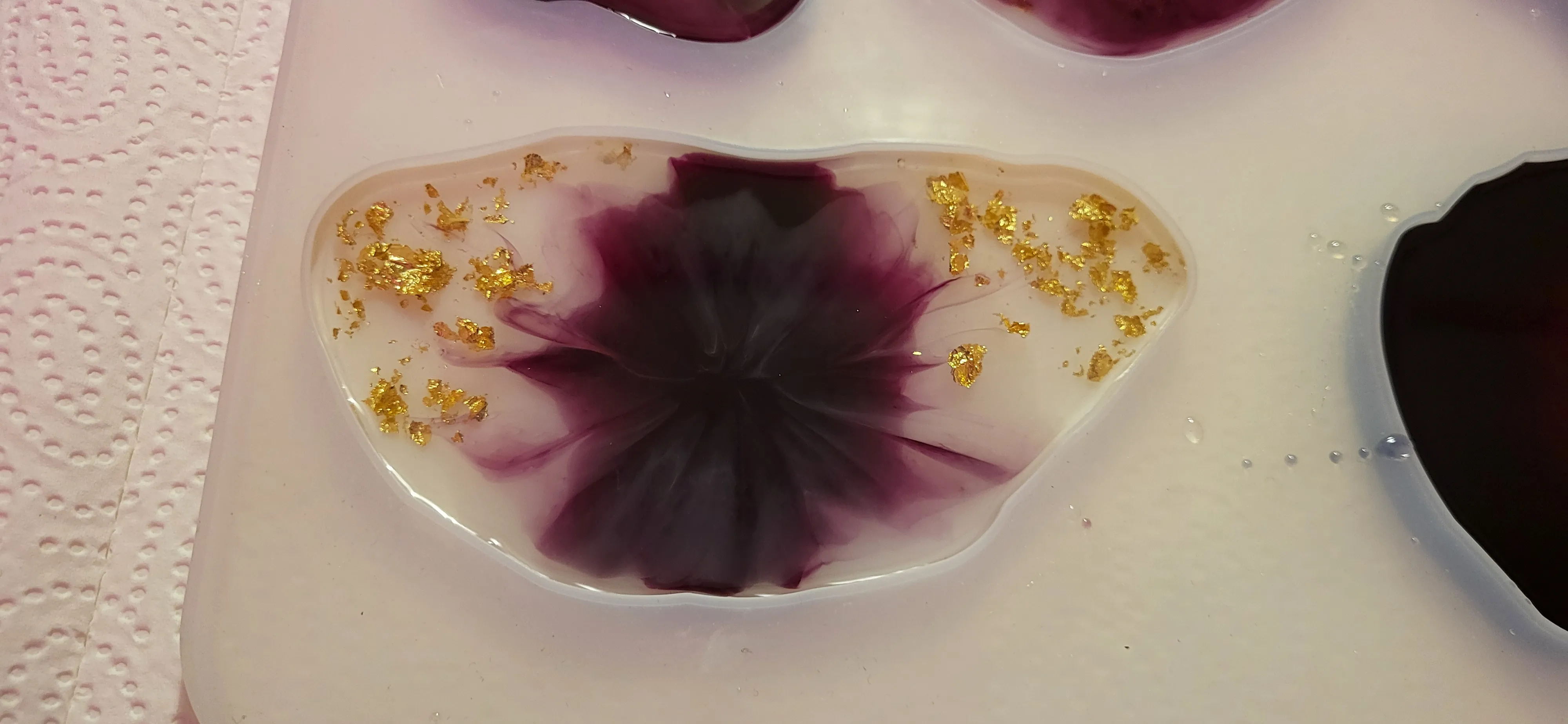 Harzkunst mit Goldflocken auf weißem Tuch.