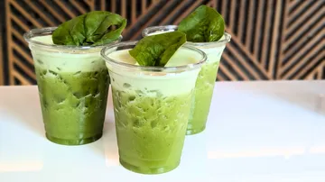 Three green smoothies topped with spinach leaves.