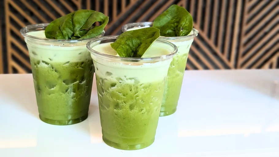 Three green smoothies topped with spinach leaves.