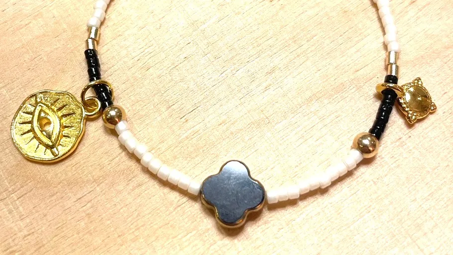 Perlenarmband mit goldenen Anhängern auf Holz.