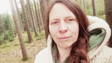 Frau im Wald mit Bäumen drumherum.