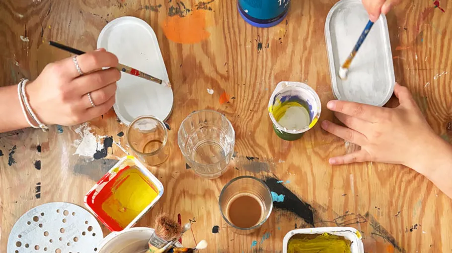 Hands painting at a colorful wooden table.