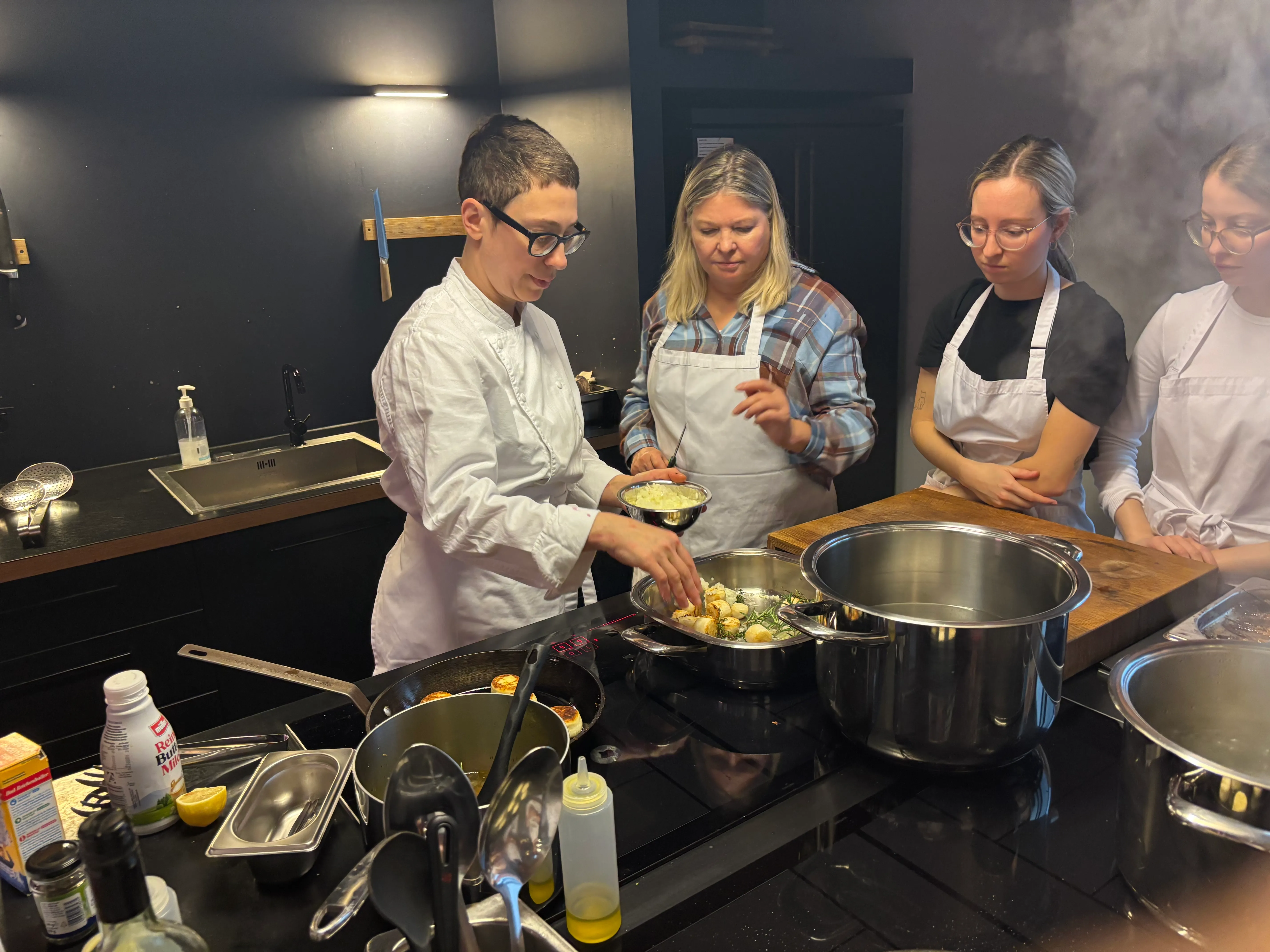 Koch unterrichtet Kochen mit drei Frauen in Küche.