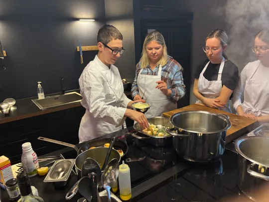 Chef teaching cooking to three women in kitchen.
