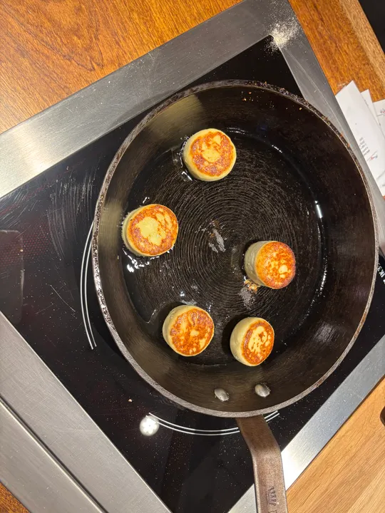 Small pancakes frying in a pan on stovetop.