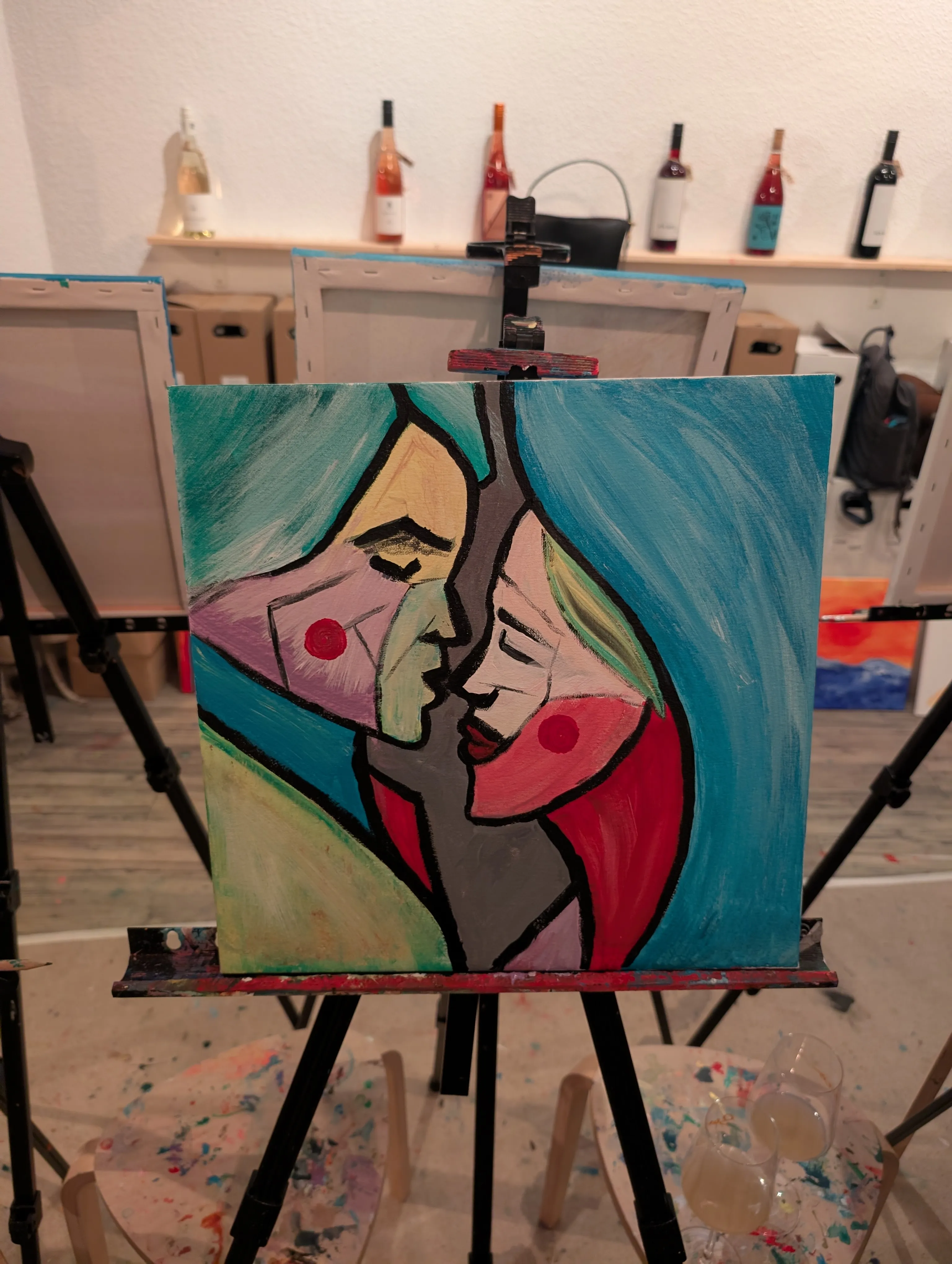 Abstract painting on easel, wine bottles in background.
