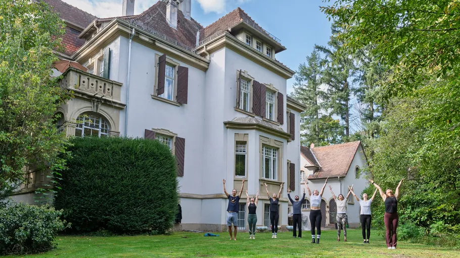 Group practicing yoga outside large house