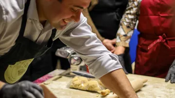 Man rolling dough in kitchen setting.