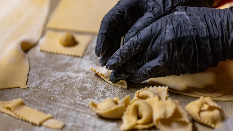 Hände machen Pasta auf bemehlter Fläche.