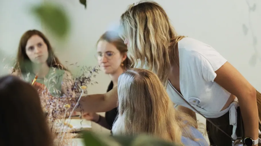 Woman teaching floral arrangement to group indoors.