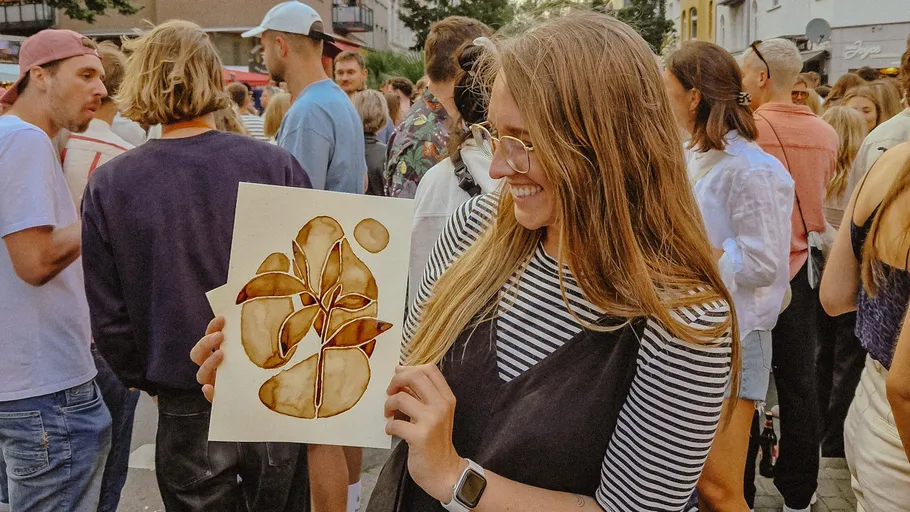Woman holding abstract painting at crowded event.