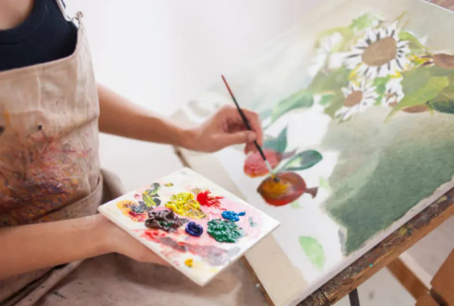 Artist painting flowers on canvas indoors.