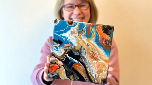 Person holding abstract colorful painting indoors.