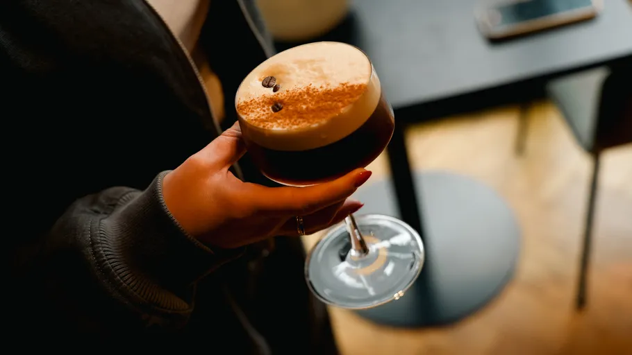 Person hält Espresso-Martini, modernes Interieur.