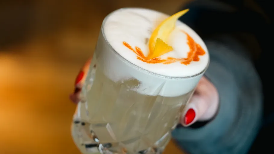 Cocktail mit Schaum und Orangendeko gehalten.
