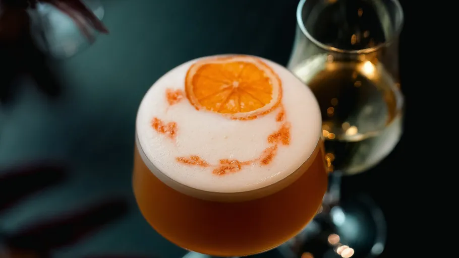 Cocktail mit Orangenscheibe und Schaum, dunkler Hintergrund.