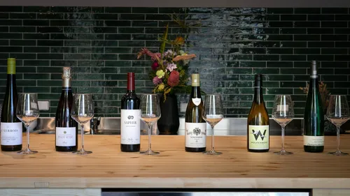 Six wine bottles with glasses on wooden counter.