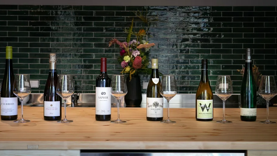 Six wine bottles with glasses on wooden counter.