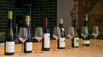 Seven wine bottles with glasses on table.