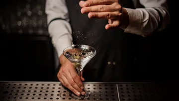 Bartender garnishing cocktail at bar counter.