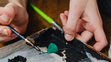 Hands mixing paint on a palette.