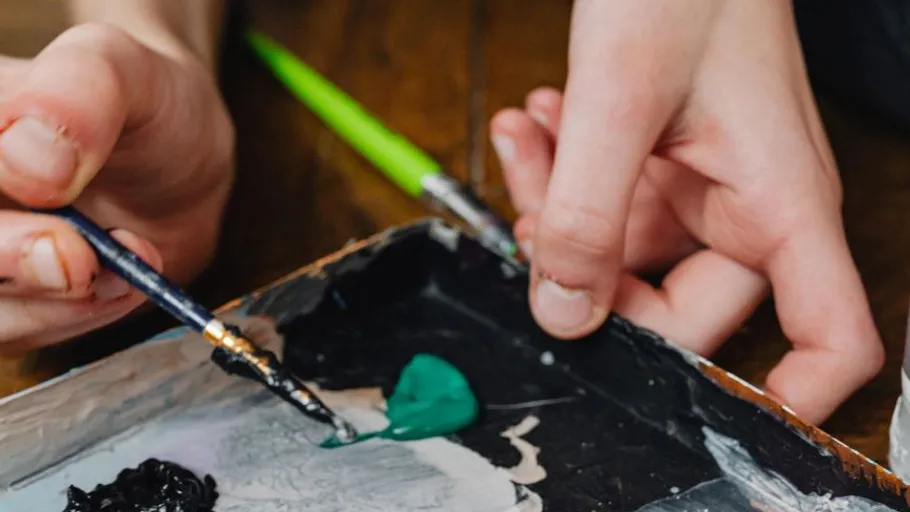 Hands mixing paint on a palette.