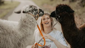 Woman smiling with two llamas on pathway.