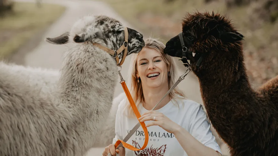 Frau lächelt mit zwei Lamas auf Weg.