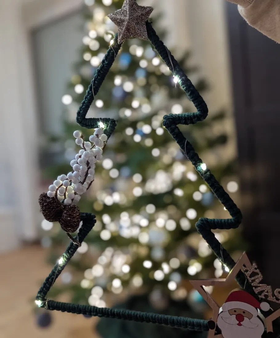 Hand hält dreieckige Weihnachtsdeko im dekorierten Raum.