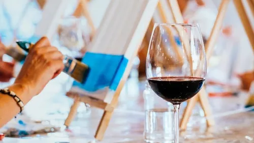 Person painting canvas, glass of wine nearby.