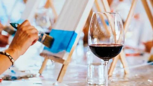 Person painting canvas, wine glass nearby.