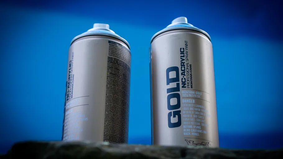 Spray paint cans on stone surface, blue background.