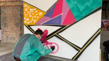 Künstler sprüht farbiges geometrisches Wandbild.