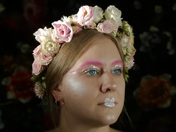 Woman with a wreath of flowers looks thoughtfully in a dark background.