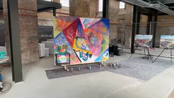 Buntes Gemälde auf Staffelei in Industrieraum.
