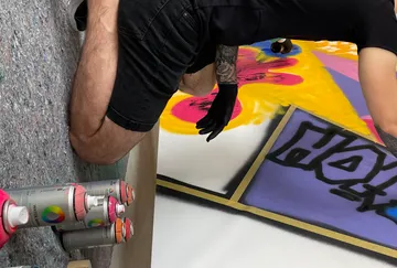 Person spray paints colorful artwork on canvas.