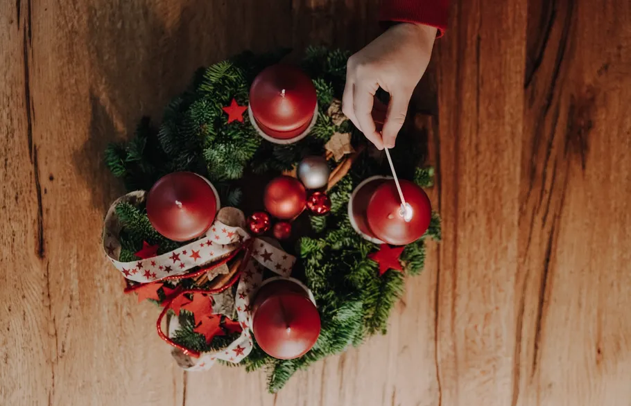 Hand zündet Kerze auf Adventskranz an.
