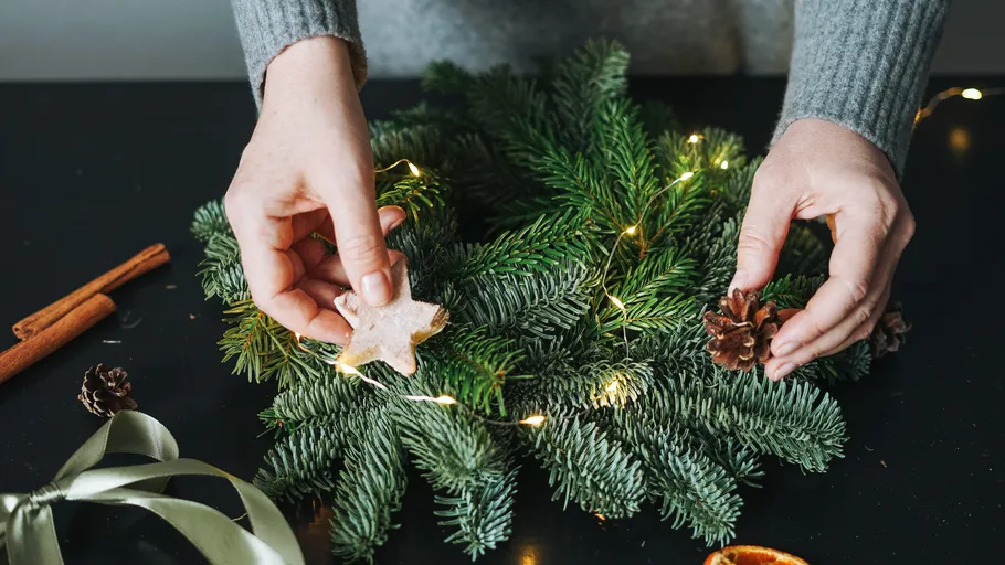 Hands decorating wreath with lights.