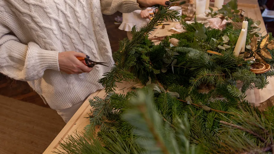 Person crafting wreath with greenery on table.