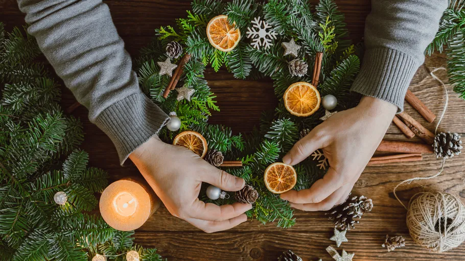 Hands arranging Christmas wreath with decorations.