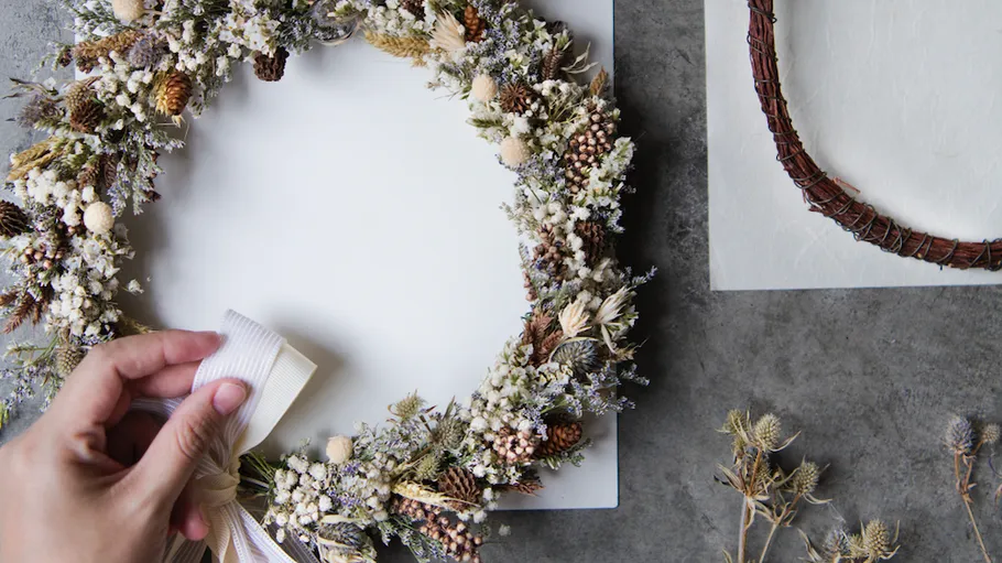 Hand arranging floral wreath on table.