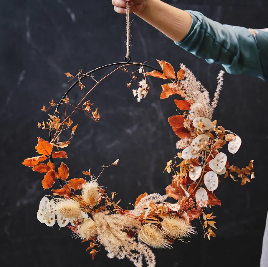 Hand hält Herbstkranz vor schwarzem Hintergrund.