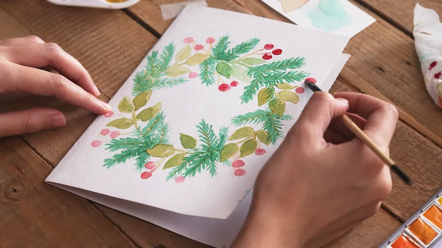 Person painting holiday card with green wreath.